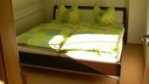 A small, single-bed room with a sloped ceiling, a wooden headboard, and a simple, unadorned wall.