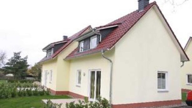 A two-story house with a red-tiled roof, a small porch, and a garden in front.
