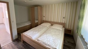 Un dormitori amb un llit de fusta, un armari i una cortina rayada.