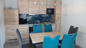 Una cucina moderna con mobili in legno, un forno a microonde e un lavello. Quattro sedie blu attorno a un tavolo di legno.