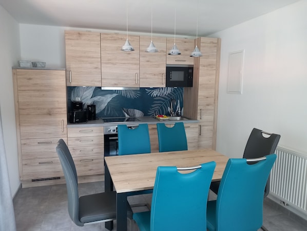 A modern kitchen with wooden cabinets, a microwave, and a sink. There are four blue chairs around a wooden table.