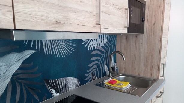 Cucina dal design moderno, con lavello in acciaio inossidabile, pensili in legno e schienale decorato con motivo foglia.