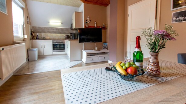 A kitchen with a TV, a dining area with a table set for two, and a living area with a sofa. - Langfeld, A. Apartment upstairs, 4P - Apartments Langfeld, Christa (Sellin)