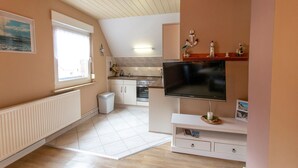A modern kitchen with a large TV, a window, and a small dining area. - Langfeld, A. Apartment upstairs, 4P - Apartments Langfeld, Christa (Sellin)