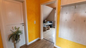 A hallway with a white door, a potted plant, and a desk in the background. - Langfeld, A. Apartment upstairs, 4P - Apartments Langfeld, Christa (Sellin)