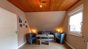 A cozy room with a wooden ceiling, a sofa, two chairs, a table, and a window. - Langfeld, A. Apartment upstairs, 4P - Apartments Langfeld, Christa (Sellin)