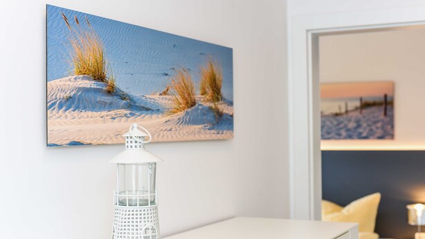 Una habitación con una consola blanca, un farol blanco y un cuadro de una playa.