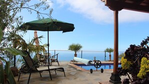 A poolside area with lounge chairs, an umbrella, and a view of the sea.