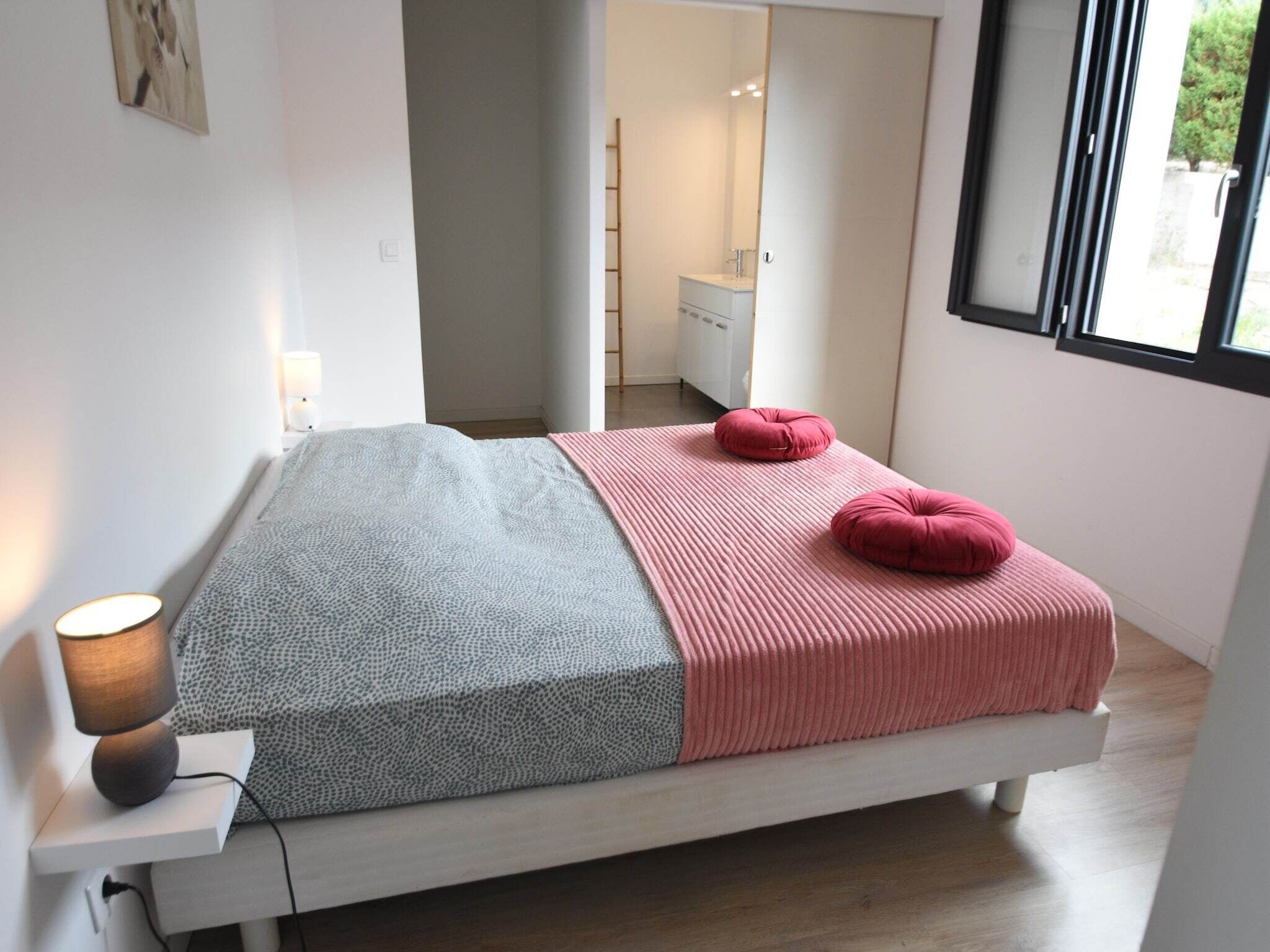 A modern bedroom with a bed, a bedside lamp, and a window.