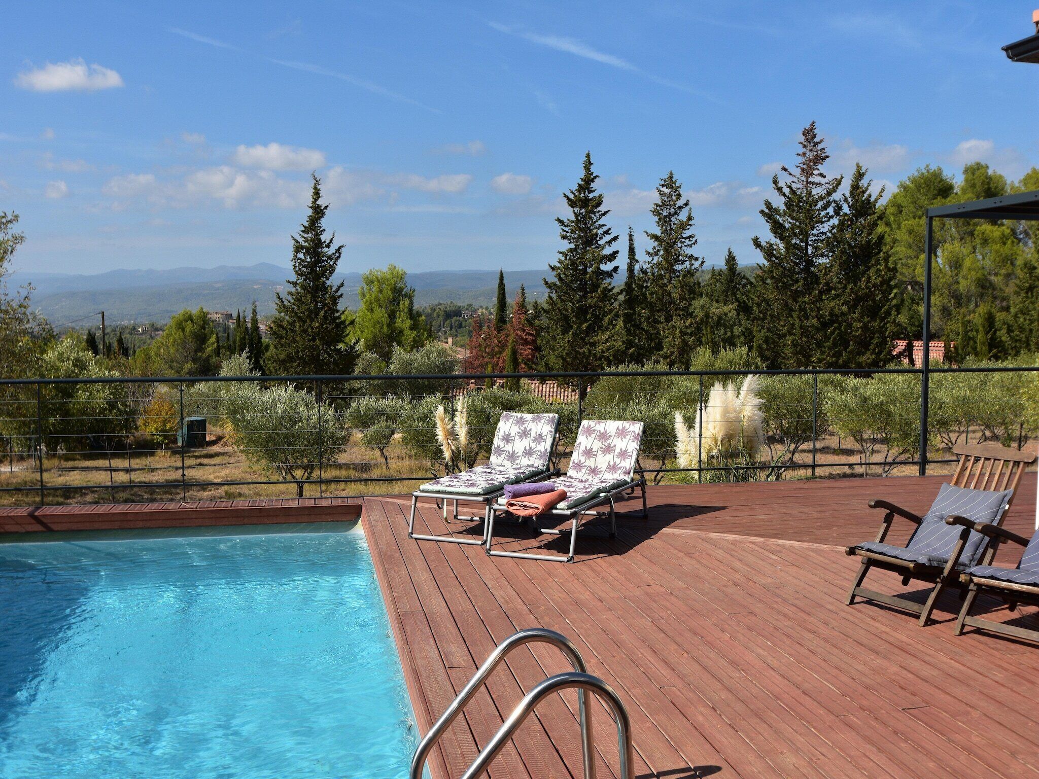Une terrasse en bois avec une piscine, des chaises longues et une vue sur les arbres et les montagnes.