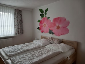 A bedroom with two beds, a radiator, a window with curtains, and a floral wall decoration.