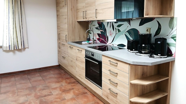 Een keuken met houten kastjes, een inbouwoven, een aanrecht met een koffiezetapparaat en een spatwand met een bloemendecor.