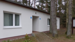 Een wit gebouw met twee genummerde ramen, een metselpad en omliggende bomen.