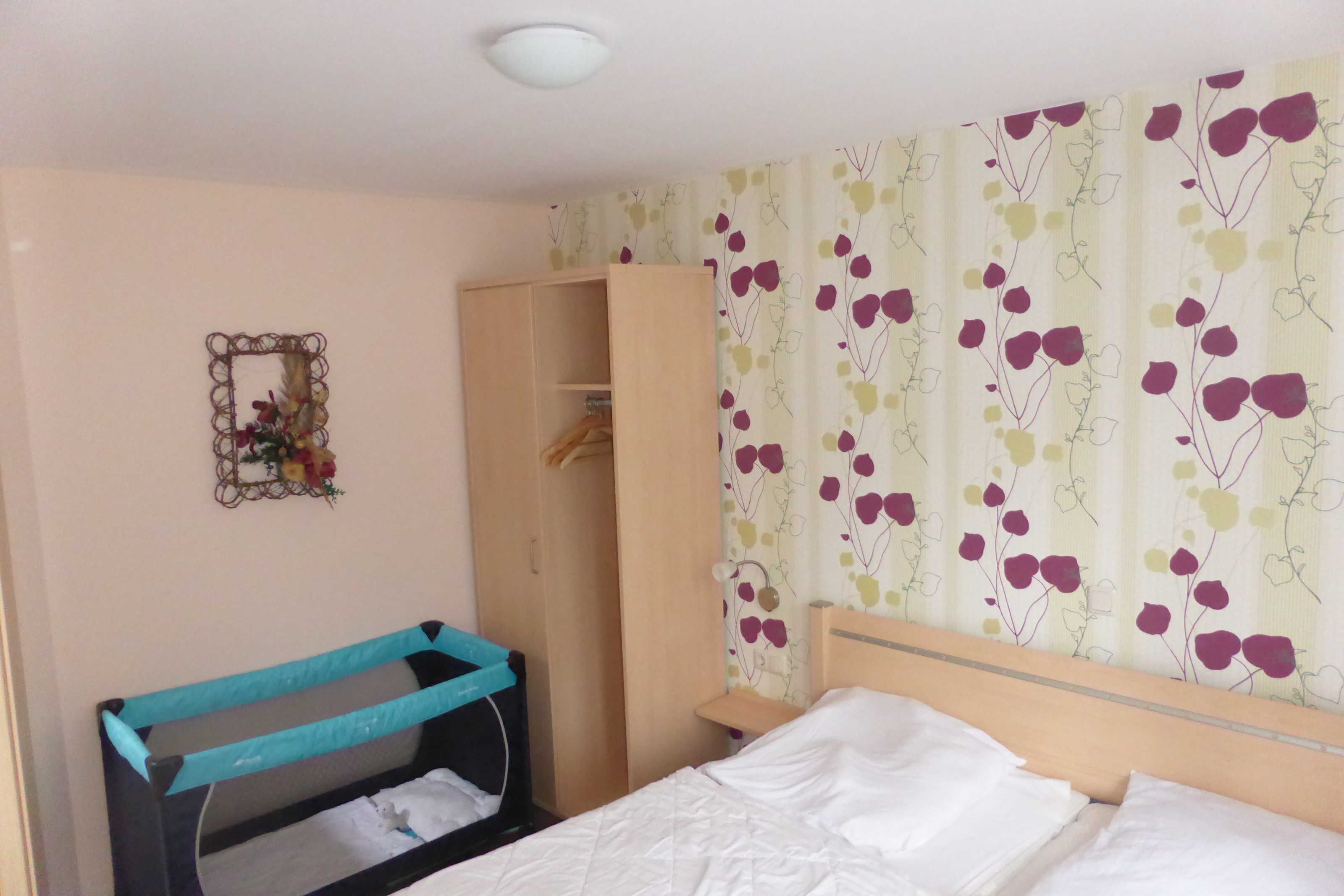 Ein Schlafzimmer mit Bett, Kleiderschrank, einem kleinen Tisch und einem Wandspiegel.