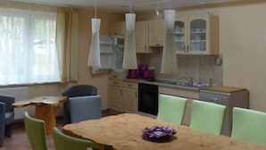 Een eetruimte met een houten tafel en groene stoelen, een keuken met lichte kasten, en een dakraam erboven.