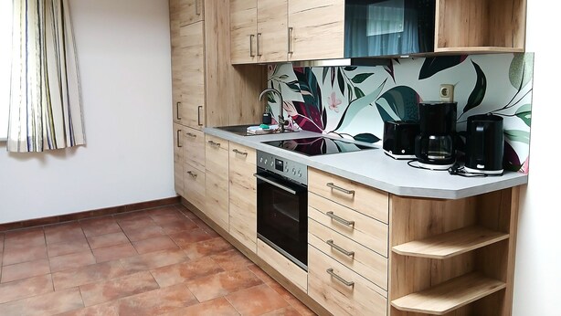 A kitchen with wooden cabinets, a built-in oven, a countertop with a coffee maker, and a backsplash with a floral design. - Room 38 - Owl's nest (Trassenheide)