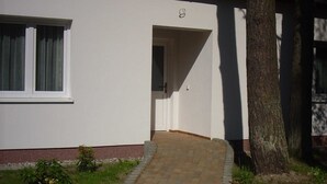 A building with a white exterior, a door, and a paved entrance. - Vacation apartment (wheelchair accessible) 41 - Käuzchenkuhle (Trassenheide)