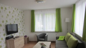 A living room with a flat-screen TV, a sofa, a coffee table, and a chair. - Vacation apartment (wheelchair accessible) 41 - Käuzchenkuhle (Trassenheide)