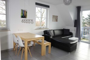 A modern living room with a wooden dining table, a black leather sofa, and a large window.