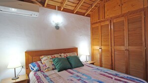 Ein Schlafzimmer mit Holzboden, einem Bett mit farbenfroher Quilttdecke, zwei Nachttischlampen, einem Nachttisch und einem Holzschrank.