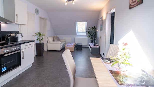 Een moderne keuken met witte kasten, een zwart fornuis, en een eethoek met een houten tafel en stoelen.