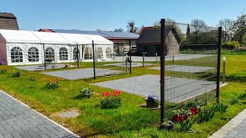 Ein überdachter Außenbereich mit einem weißen Zelt, einem eingezäunten Spielplatz und einem Gebäude mit rotem Dach.