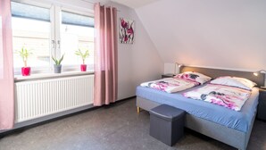 Een slaapkamer met een bed, nachtkastje, lamp, radiator, raam met gordijnen en potplanten.
