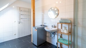 Een moderne badkamer met een douche, wastafel, spiegel en handdoekhouder.