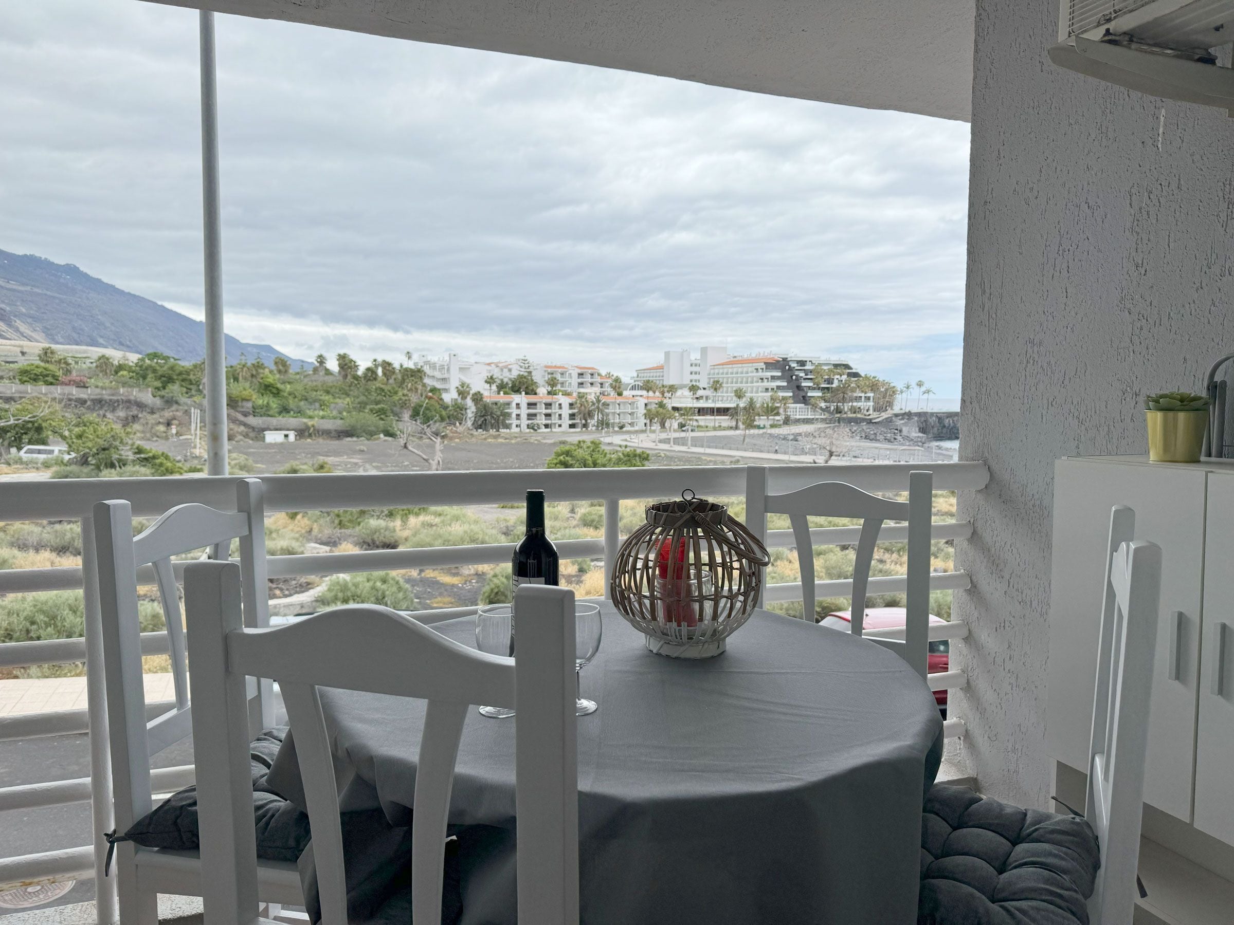 Een balkon met een tafel voor twee, uitkijkend op een kustlandschap met gebouwen in de verte.