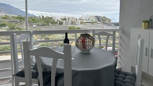 A balcony with a table set for two, overlooking a coastal landscape with buildings in the distance. - Apartment Sol y Playa (Puerto de Naos)