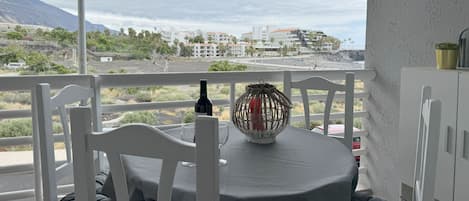 A balcony with a table set for two, overlooking a coastal landscape with buildings in the distance.