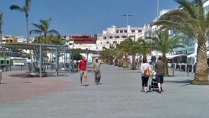 A pedestrian walkway with palm trees, a covered seating area, and buildings in the background. - Apartment Sol y Playa (Puerto de Naos)