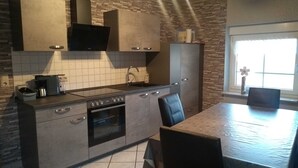 Une cuisine moderne avec des meubles gris, un four encastré, un four à micro-ondes et une machine à café. Une fenêtre offre une vue sur l’extérieur.