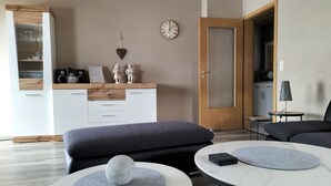 Un salon moderne comprenant un canapé, deux tables rondes, un meuble en bois et une horloge murale.