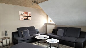 Un salon moderne avec un canapé d’angle, deux petites tables basses rondes et une petite table d’appoint.