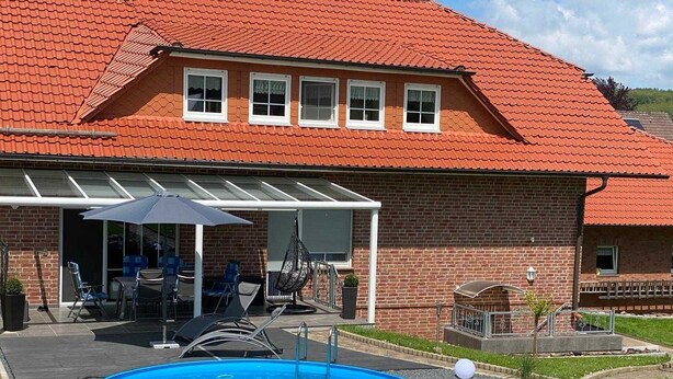 Une maison avec une piscine, du mobilier de jardin et un espace extérieur aménagé avec un coin salon couvert.
