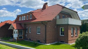 Une maison à deux étages, construite en briques, avec un toit recouvert de tuiles rouges, un balcon et une pelouse bien entretenue.