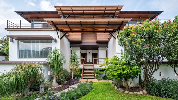 A modern two-story house with a covered entrance, a staircase, and a well-maintained garden. - The Pig House Khao Yai (Pak Chong)