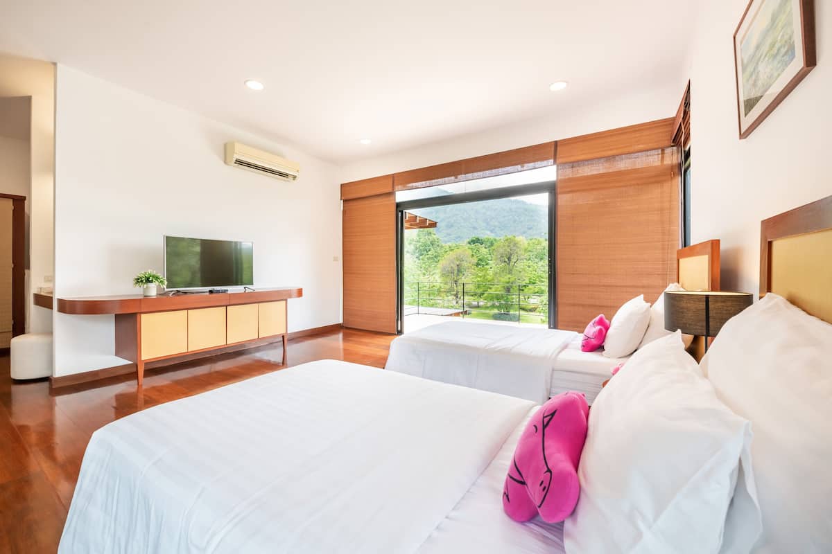 A modern hotel room with two beds, a TV, a wooden cabinet, and a large window offering a view of greenery.