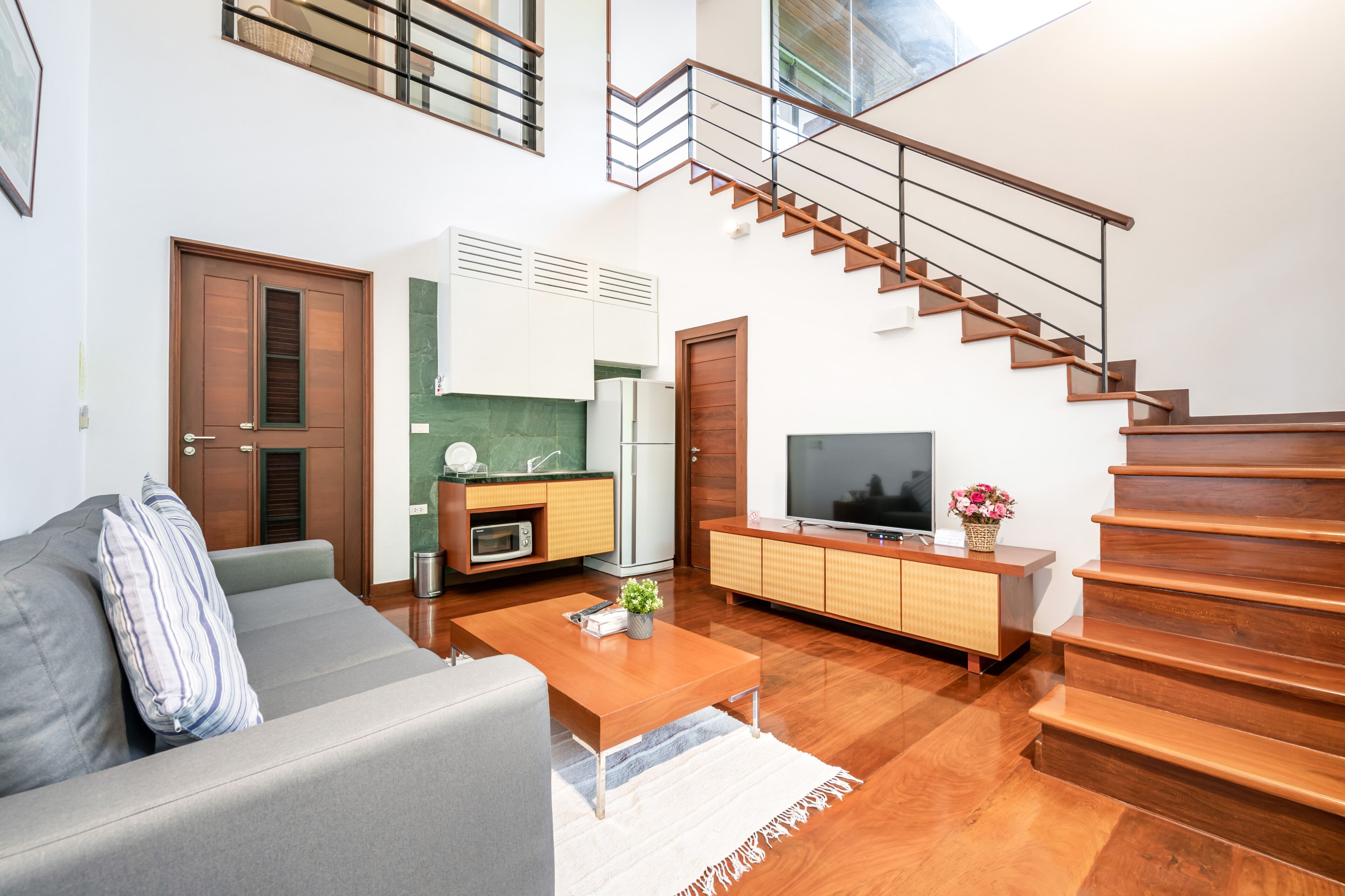 A modern living room with a sofa, coffee table, TV, and wooden staircase.