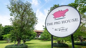 A sign for "The Pig House by The Gallery Khaoyai" in a landscaped garden with trees and a building in the background. - The Pig House Khao Yai (Pak Chong)