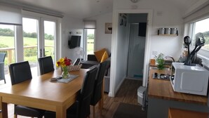Een moderne keuken met een magnetron, spoelbak en bestek. Er is een eethoek met een tafel en stoelen, en een aan de muur bevestigde televisie.