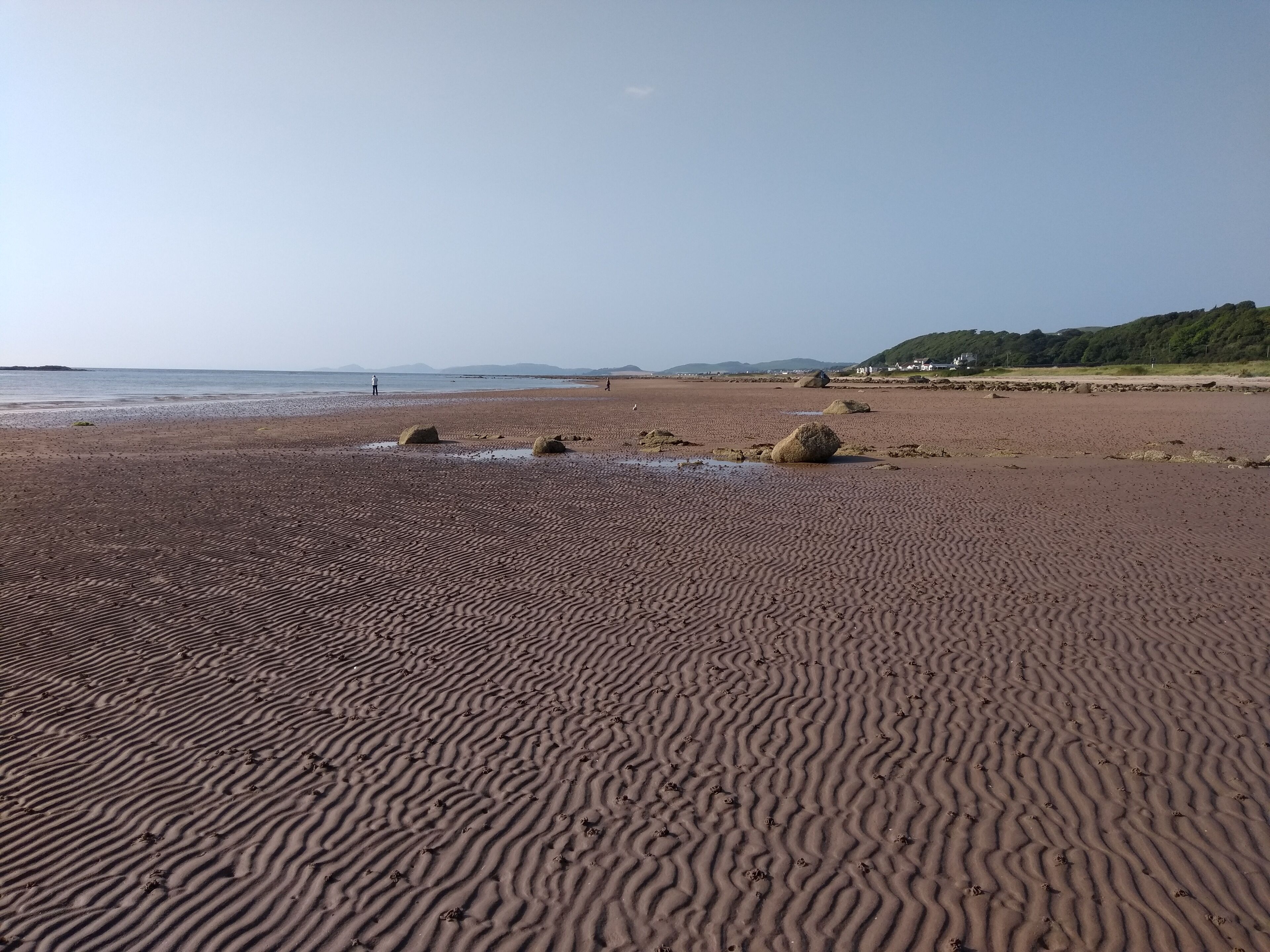 A sandy beach with visible footprints and rocks.