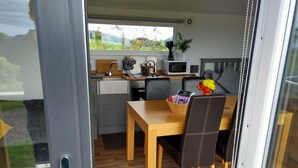 Een kleine keuken met een houten tafel en stoelen, een magnetron, waterkoker en een kleine plant in pot.