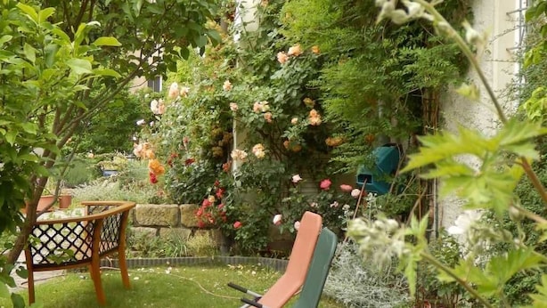 Ein Garten mit zwei Liegestühlen, einem Holztisch und verschiedenen Pflanzen und Blumen.