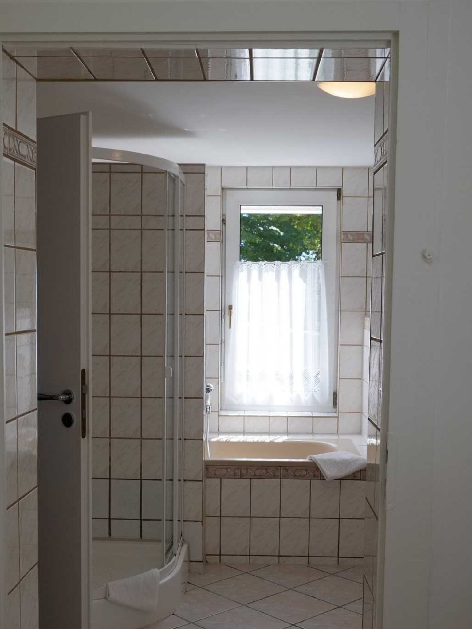 Et badeværelse med bruser, et vindue med gardin og et badekar.