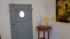 Ein Zimmer mit einer blauen Tür, einem Holzstuhl, einem kleinen Tisch mit einer Lampe und einem Bild an der Wand.