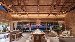 A spacious indoor area with a wooden ceiling, a dining table set for six, and a bar area with stools. - The Pines (Takua Thung)