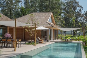 A modern poolside area with a wooden deck, lounge chairs, and umbrellas.