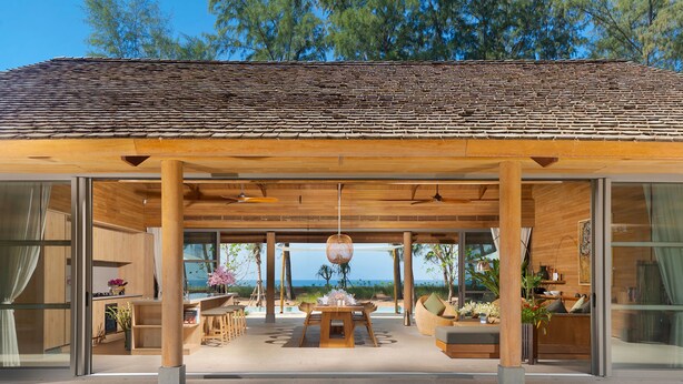 A modern outdoor lounge area with a wooden ceiling and large glass doors, overlooking a beach. - The Pines (Takua Thung)